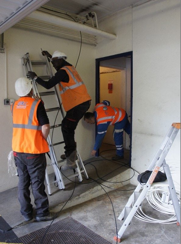 Des opérateurs s'apprêtent à faire passer la fibre par la colonne montante d'un immeuble. 